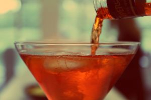 A bottle pouring orange liquid into a martini glass